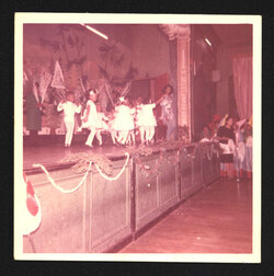 Photograph of class of young children performing on stage with teacher